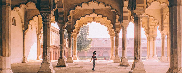A person in modern fashion, turns to look back at the camera while wandering through the classic architectural structures at in India.