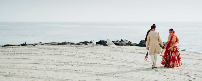Hindu wedding couple walks along the ocean shore